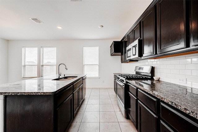 kitchen with appliances with stainless steel finishes, tasteful backsplash, an island with sink, sink, and dark stone countertops