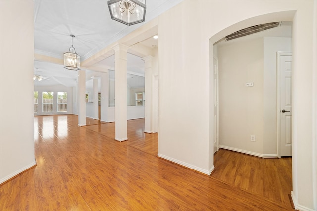 empty room with ornate columns, ornamental molding, ceiling fan with notable chandelier, and hardwood / wood-style floors