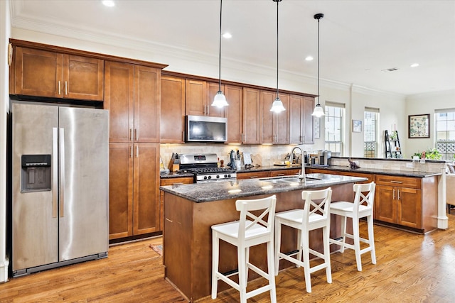 kitchen with sink, dark stone countertops, hanging light fixtures, stainless steel appliances, and a center island with sink