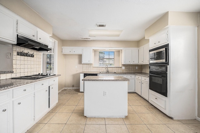 kitchen featuring stainless steel microwave, black oven, sink, white cabinets, and a center island