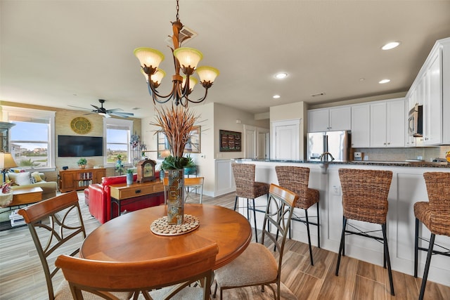 dining area featuring ceiling fan with notable chandelier and light hardwood / wood-style floors