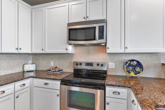 kitchen with appliances with stainless steel finishes, white cabinets, backsplash, and dark stone counters