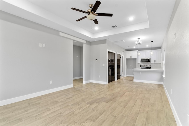 unfurnished living room with ceiling fan, a raised ceiling, and light hardwood / wood-style floors