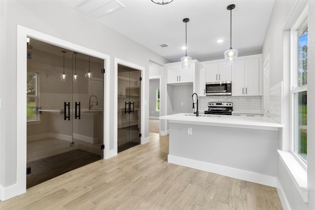 kitchen with appliances with stainless steel finishes, white cabinets, pendant lighting, light hardwood / wood-style floors, and backsplash