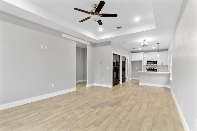 unfurnished living room featuring a tray ceiling, ceiling fan, and light wood-type flooring