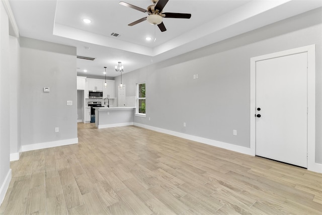 unfurnished living room featuring a tray ceiling, recessed lighting, light wood-style floors, ceiling fan, and baseboards