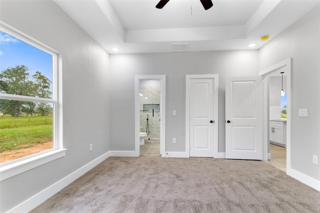 unfurnished bedroom featuring ceiling fan, light colored carpet, a tray ceiling, and ensuite bath