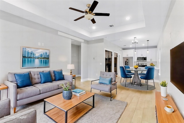 living area featuring baseboards, a raised ceiling, a ceiling fan, light wood-style flooring, and recessed lighting