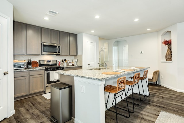 kitchen featuring sink, appliances with stainless steel finishes, light stone countertops, an island with sink, and dark hardwood / wood-style flooring