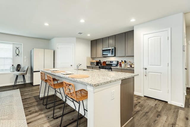 kitchen featuring stainless steel appliances, an island with sink, a breakfast bar, and dark hardwood / wood-style flooring