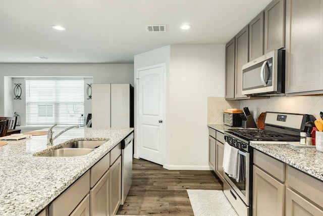 kitchen featuring dark wood-type flooring, sink, tasteful backsplash, stainless steel appliances, and light stone countertops