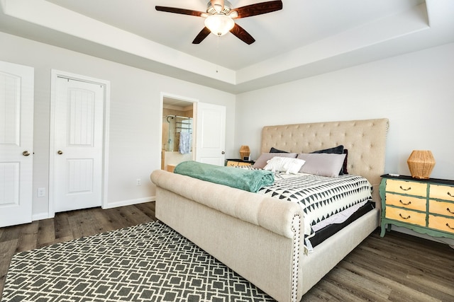 bedroom featuring dark hardwood / wood-style flooring, a tray ceiling, ensuite bath, and ceiling fan