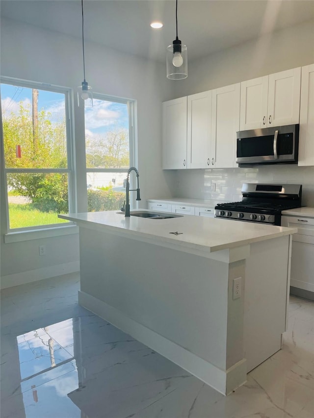 kitchen featuring stainless steel appliances, white cabinetry, a kitchen island with sink, and decorative light fixtures