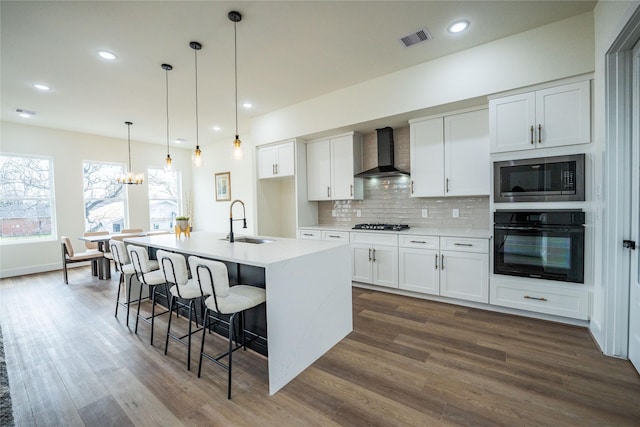 kitchen featuring white cabinetry, wall chimney range hood, oven, and a center island with sink