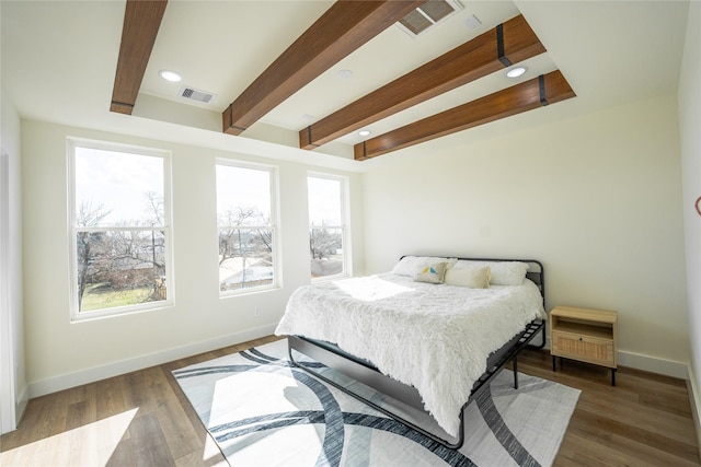 bedroom with multiple windows, hardwood / wood-style floors, and beam ceiling