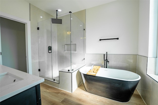 bathroom featuring vanity, hardwood / wood-style flooring, plus walk in shower, and tile walls