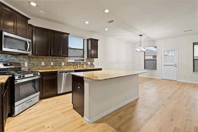 kitchen featuring appliances with stainless steel finishes, pendant lighting, tasteful backsplash, sink, and a center island