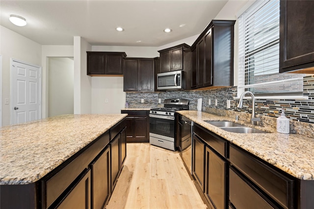 kitchen with sink, light stone counters, light hardwood / wood-style flooring, stainless steel appliances, and backsplash