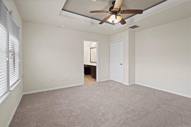 unfurnished bedroom featuring multiple windows, light colored carpet, a raised ceiling, and ensuite bathroom