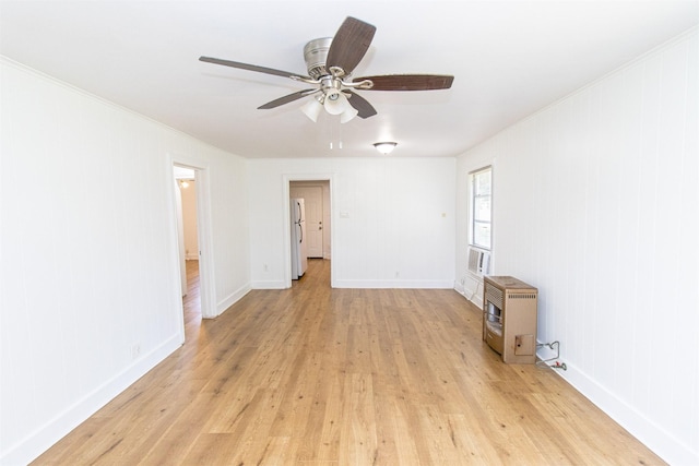 empty room with ceiling fan, light wood-style flooring, baseboards, heating unit, and crown molding