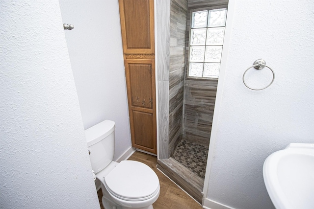 bathroom with a stall shower, a textured wall, toilet, wood finished floors, and a sink