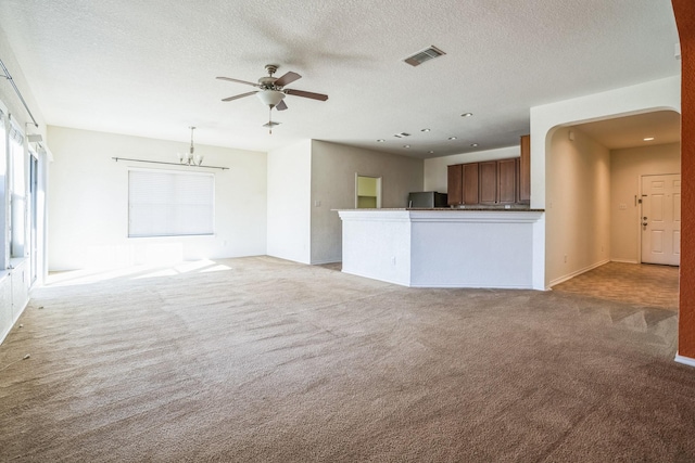 unfurnished living room featuring light carpet, ceiling fan with notable chandelier, and a textured ceiling