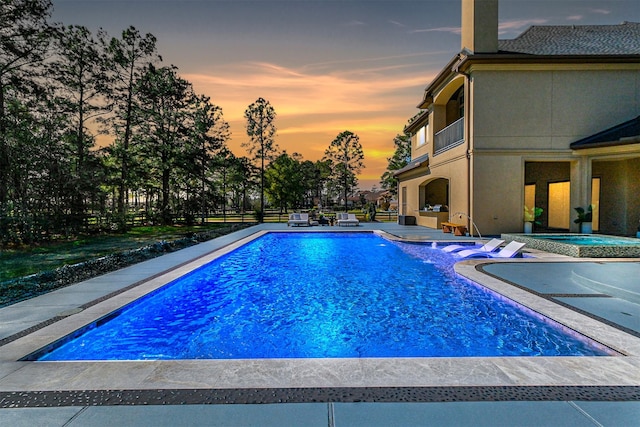 pool at dusk with a patio area, an outdoor pool, and a hot tub