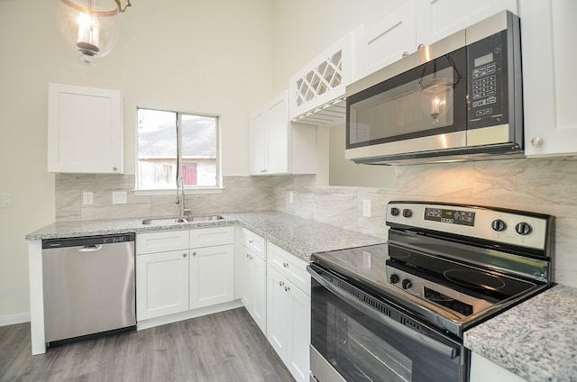 kitchen with sink, stainless steel appliances, light stone countertops, white cabinets, and light wood-type flooring