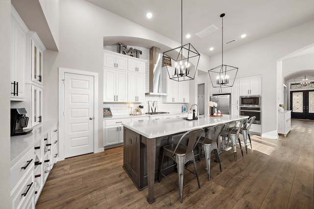 kitchen featuring white cabinetry, appliances with stainless steel finishes, a kitchen breakfast bar, a large island, and wall chimney range hood