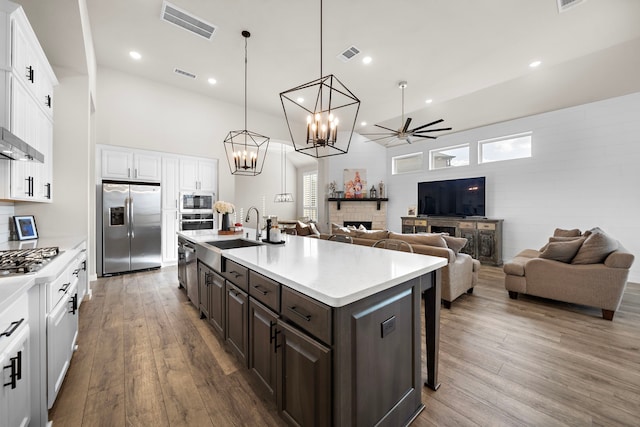 kitchen featuring a breakfast bar, white cabinetry, dark brown cabinets, stainless steel appliances, and a kitchen island with sink