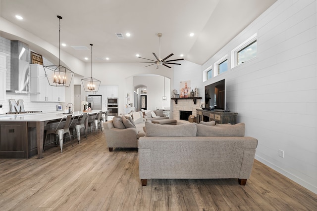 living room featuring sink, high vaulted ceiling, a stone fireplace, and light hardwood / wood-style floors