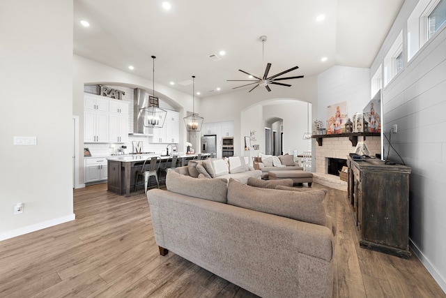 living room with wood-type flooring, high vaulted ceiling, ceiling fan, and a fireplace