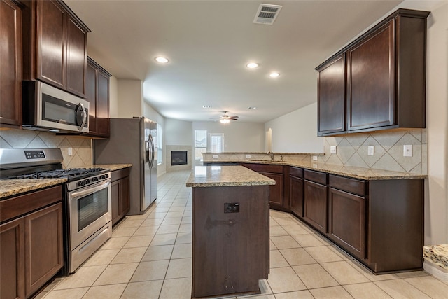 kitchen featuring stainless steel appliances, light stone countertops, a center island, and kitchen peninsula