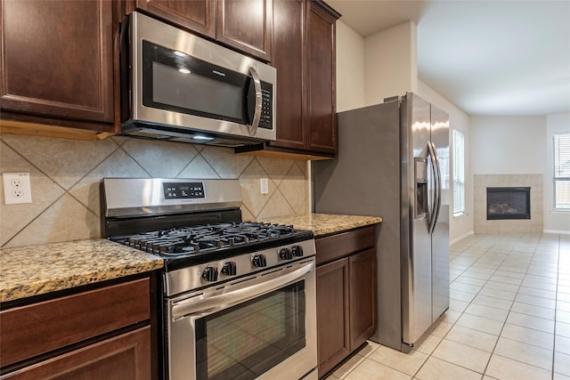 kitchen featuring light stone counters, tasteful backsplash, light tile patterned floors, a tile fireplace, and stainless steel appliances