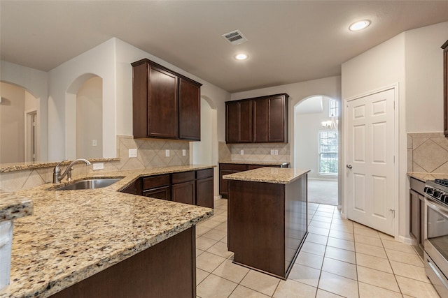 kitchen with sink, stainless steel stove, dark brown cabinets, a center island, and light stone countertops