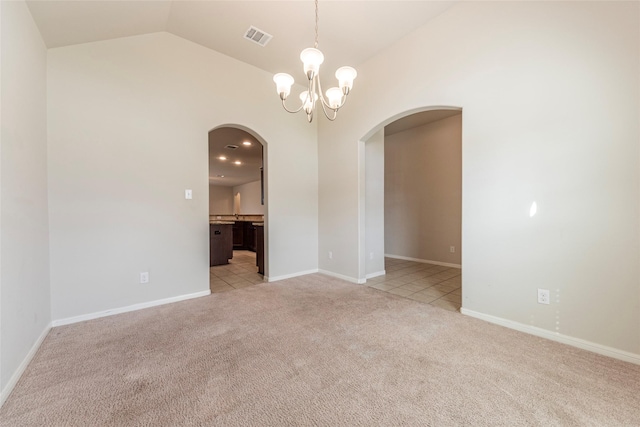 carpeted empty room with a notable chandelier and vaulted ceiling