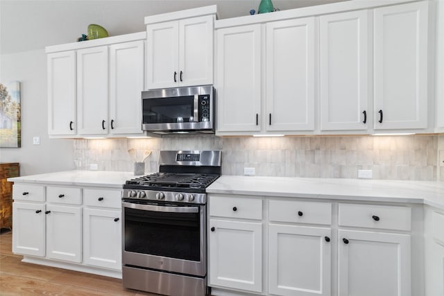 kitchen with white cabinets, stainless steel appliances, decorative backsplash, and light hardwood / wood-style flooring