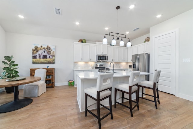 kitchen featuring a center island with sink, appliances with stainless steel finishes, a breakfast bar, white cabinetry, and decorative light fixtures