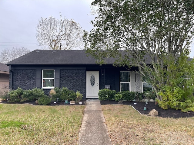 ranch-style house featuring roof with shingles and a front yard