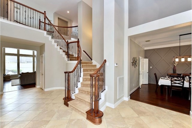 foyer entrance featuring visible vents, baseboards, a towering ceiling, stairway, and ornamental molding