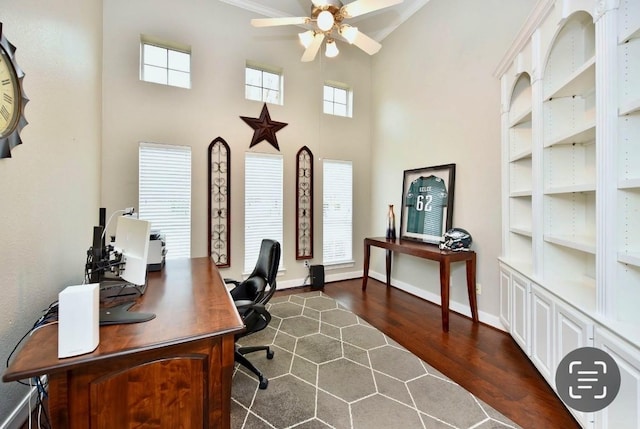 home office with a ceiling fan, dark wood finished floors, a towering ceiling, and baseboards