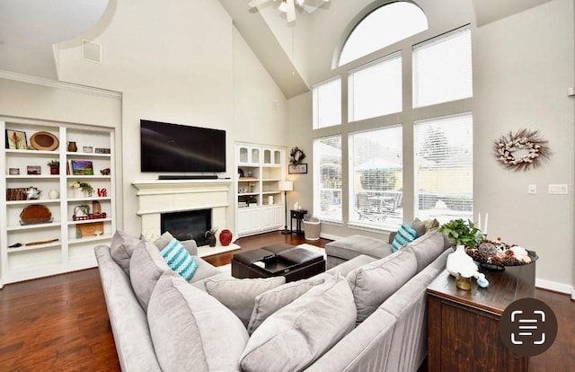 living room with baseboards, visible vents, dark wood finished floors, a glass covered fireplace, and a towering ceiling