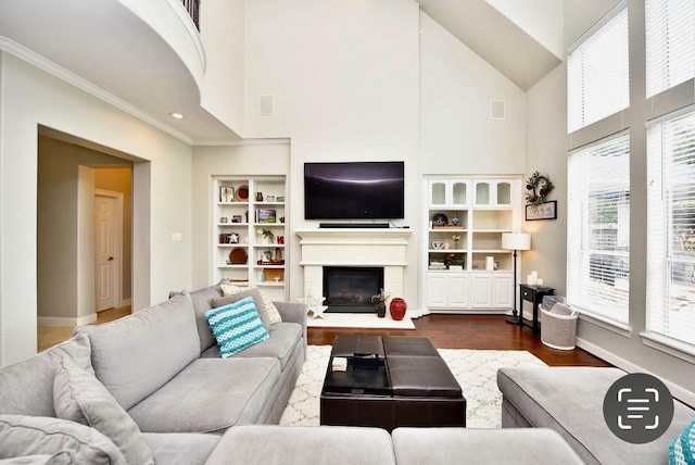 living area featuring dark wood-style floors, built in shelves, ornamental molding, a glass covered fireplace, and baseboards