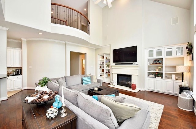 living room with built in shelves, dark wood finished floors, ornamental molding, a glass covered fireplace, and baseboards