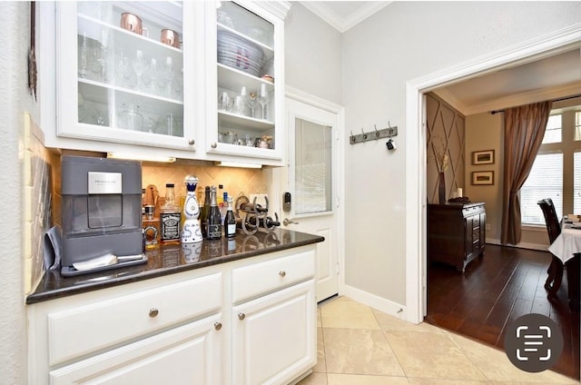 bar with baseboards, crown molding, a bar, backsplash, and light tile patterned flooring