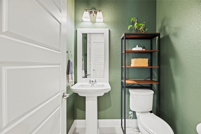 half bath featuring toilet, a textured wall, and baseboards