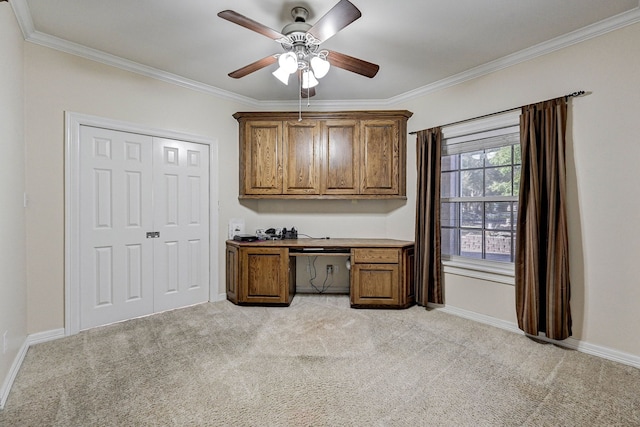 unfurnished office with ceiling fan, ornamental molding, built in desk, and light carpet