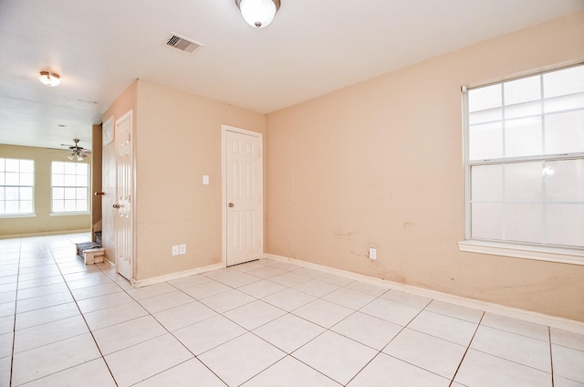 spare room with light tile patterned floors, a ceiling fan, visible vents, and baseboards