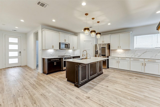 kitchen with sink, white cabinetry, stainless steel appliances, an island with sink, and decorative light fixtures