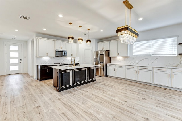 kitchen featuring appliances with stainless steel finishes, white cabinets, hanging light fixtures, light hardwood / wood-style floors, and a center island with sink